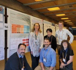 A group of researchers pose in front of a research poster.